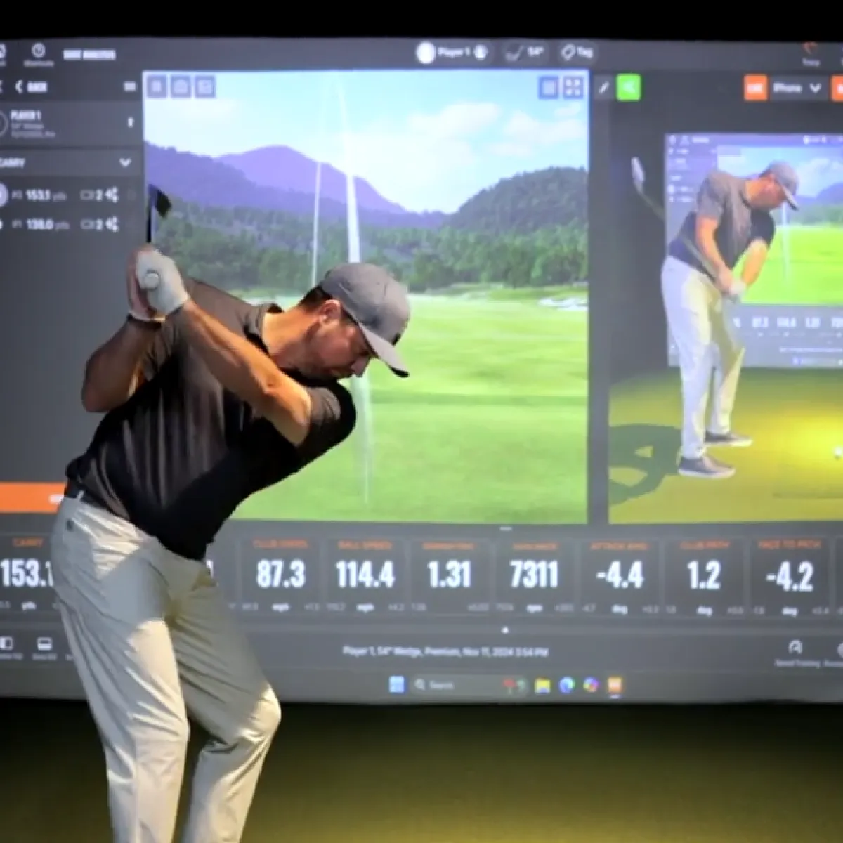 Golfer mid-backswing indoors before a golf-simulator screen showing a virtual course and swing metrics.