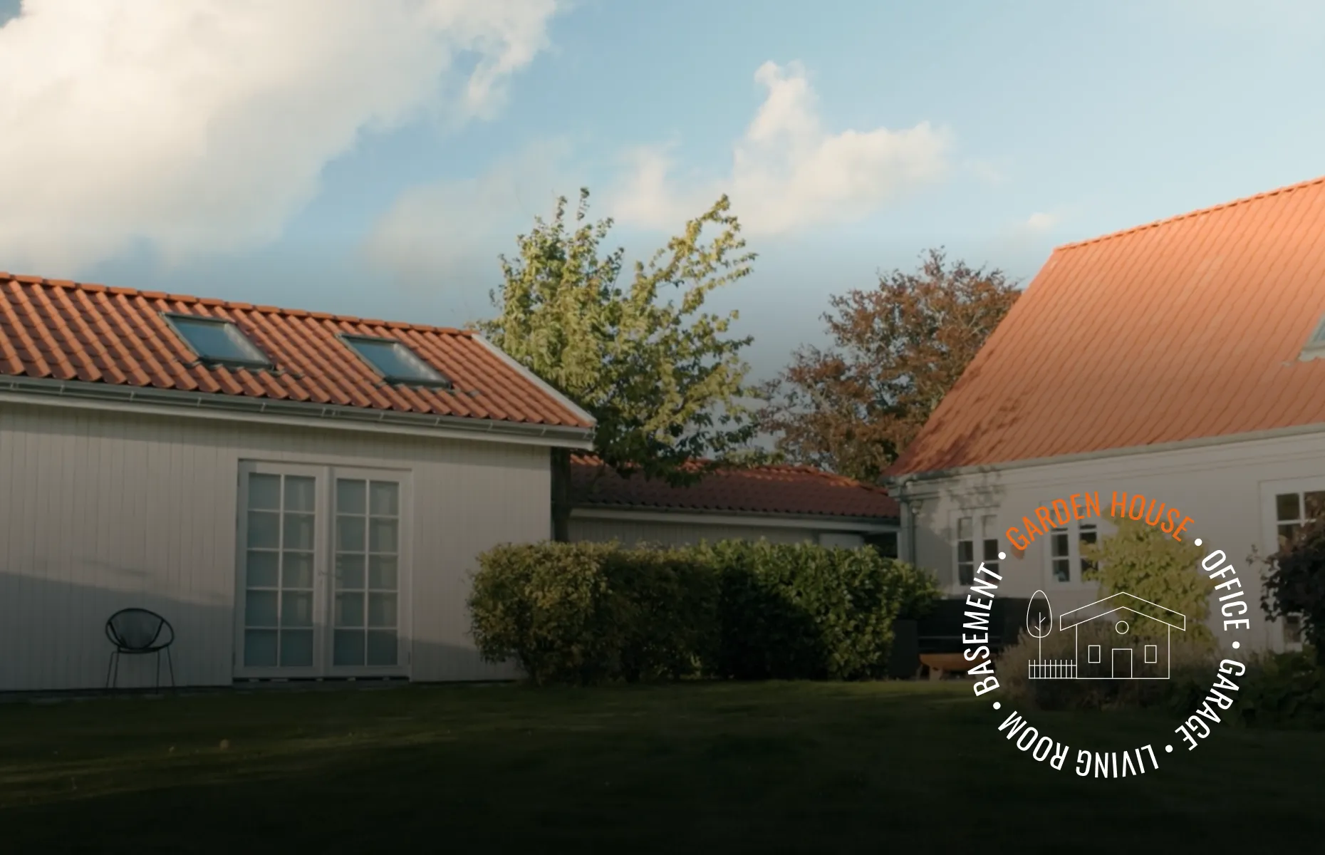 Two white houses with red roofs and skylights, surrounded by greenery and a cloudy sky. Circular text overlay with labels like "Garden House."