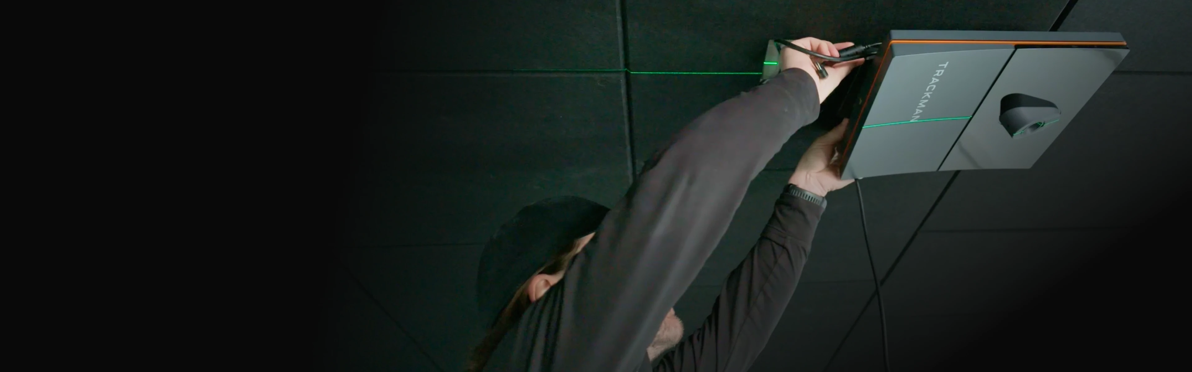 Person installing a TrackMan device on a ceiling, aligning it with a green laser line.