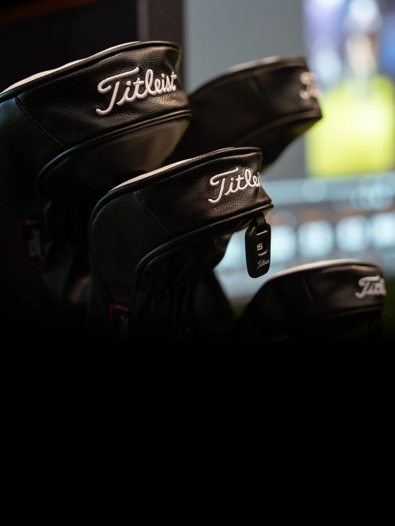 Close-up of black Titleist golf club headcovers with white embroidery, numbered tag "6" visible, against a blurred background.