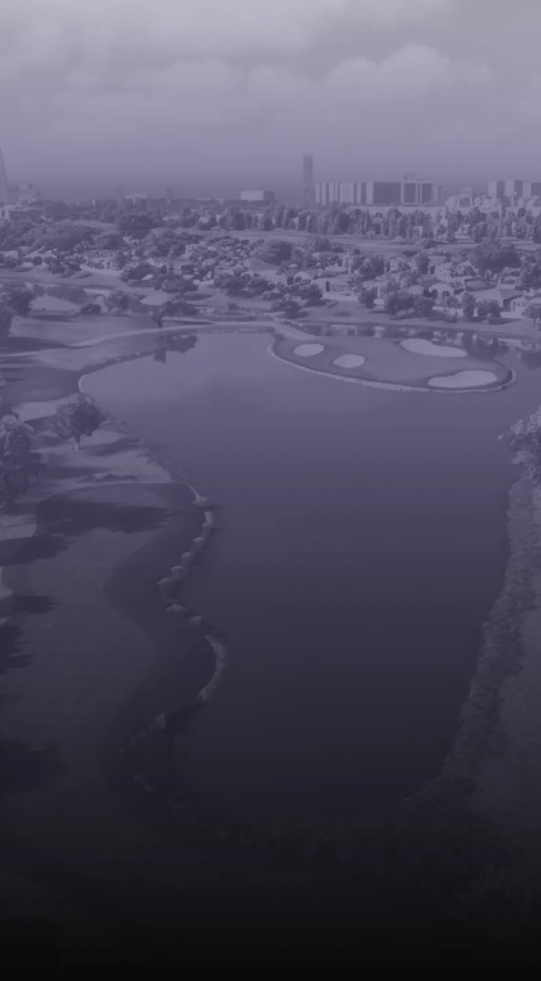 Aerial view of a golf course with a large water feature, surrounded by trees and buildings in the distance under a cloudy sky.