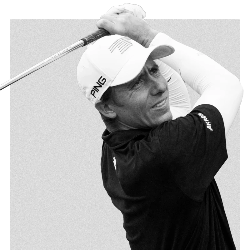 Golfer in a cap and long sleeve takes a swing, eyes focused, with a club above the shoulder.