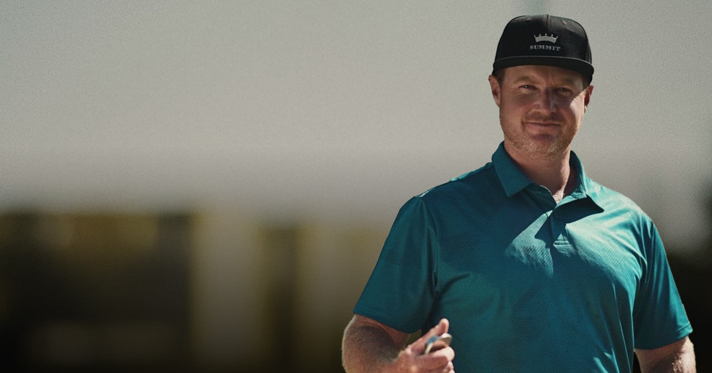 Dana Dahlquist in a teal polo and black cap stands outdoors, holding a golf club, with a blurred background.
