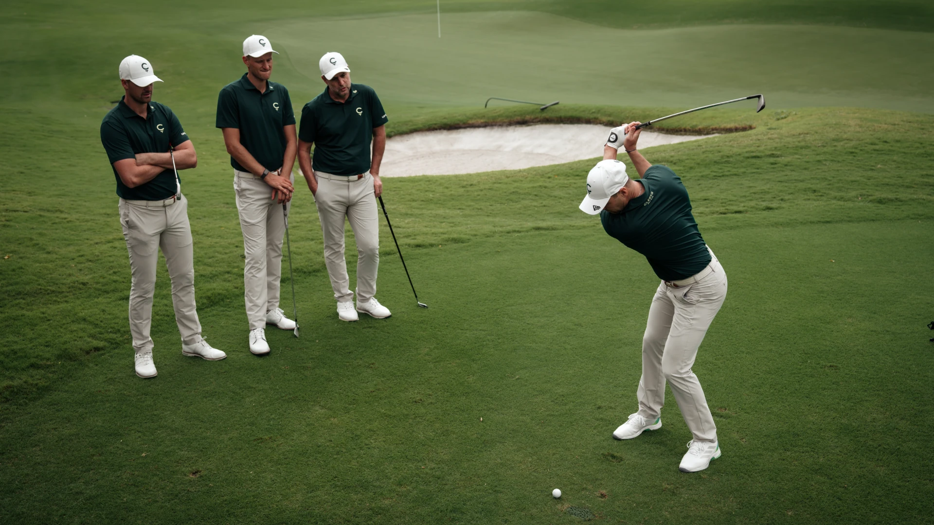 A golfer swings a club on a green, observed by three others in matching outfits with "C" logos on their caps and shirts.