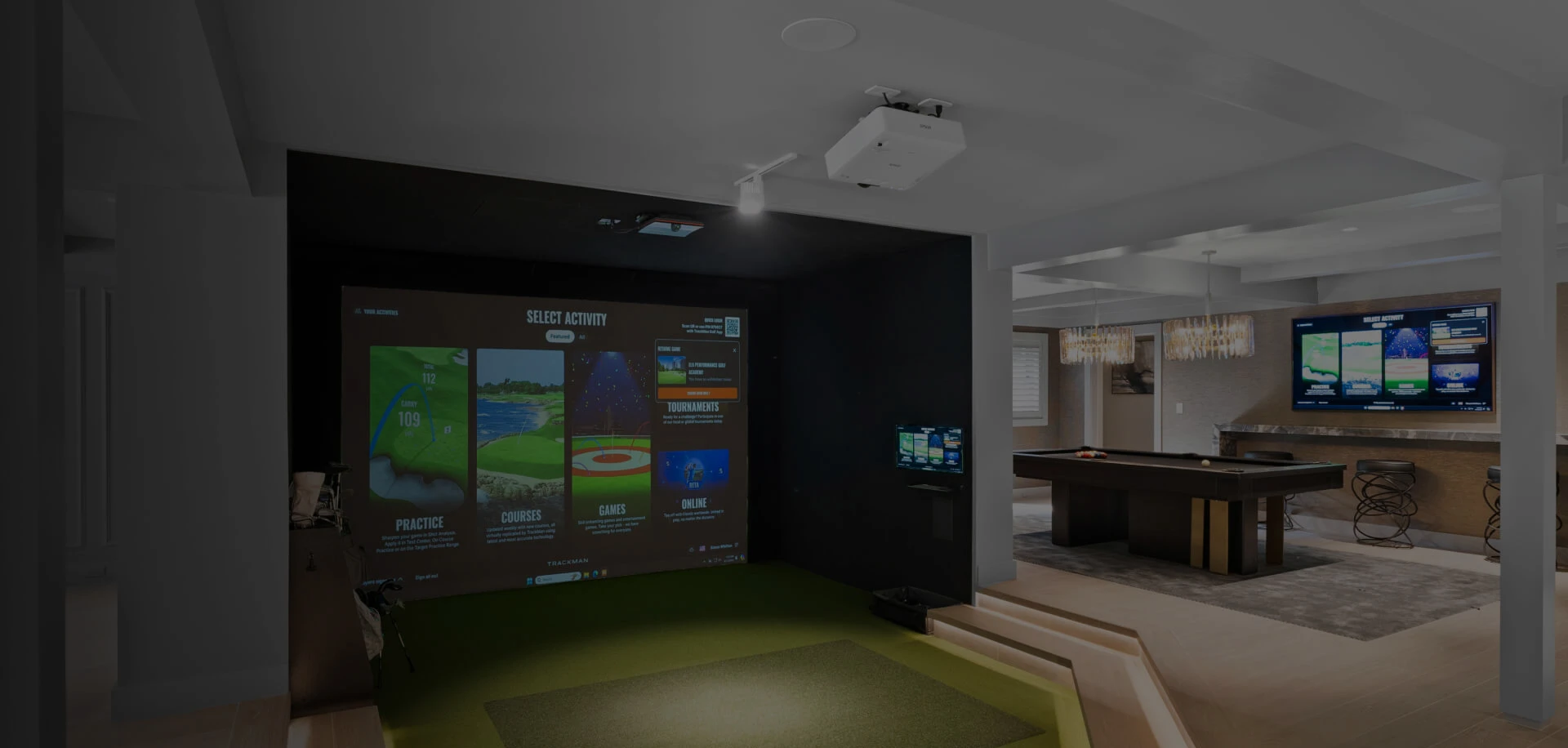 Basement entertainment room with golf simulator (projected screen and turf), pool table, wall TV and bar seating.