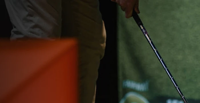 Person holding a golf club, standing on green turf, partially visible.