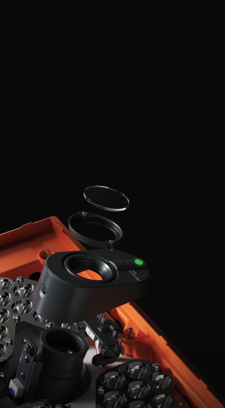 Close-up of a black camera lens assembly with an orange base, showing disassembled components against a black background.