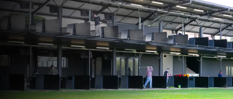 Two-level driving range with people practicing golf swings in individual bays. The facility is covered with a roof.
